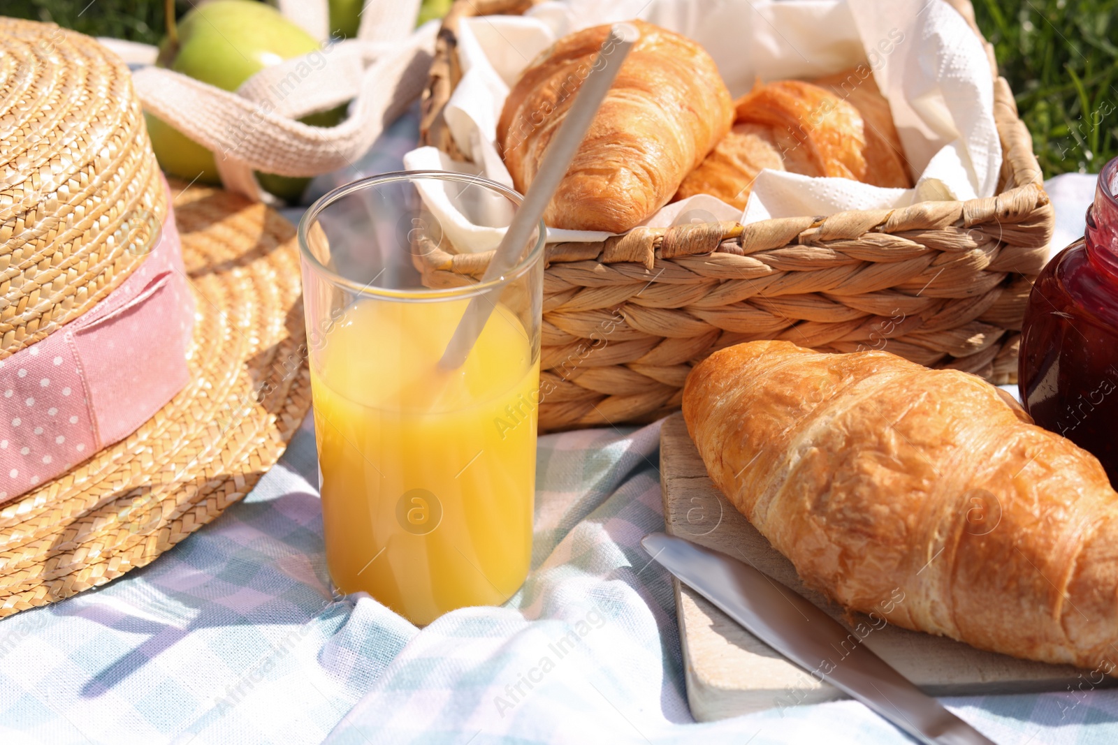 Photo of Blanket with juice, jam and croissants for picnic on green grass, closeup