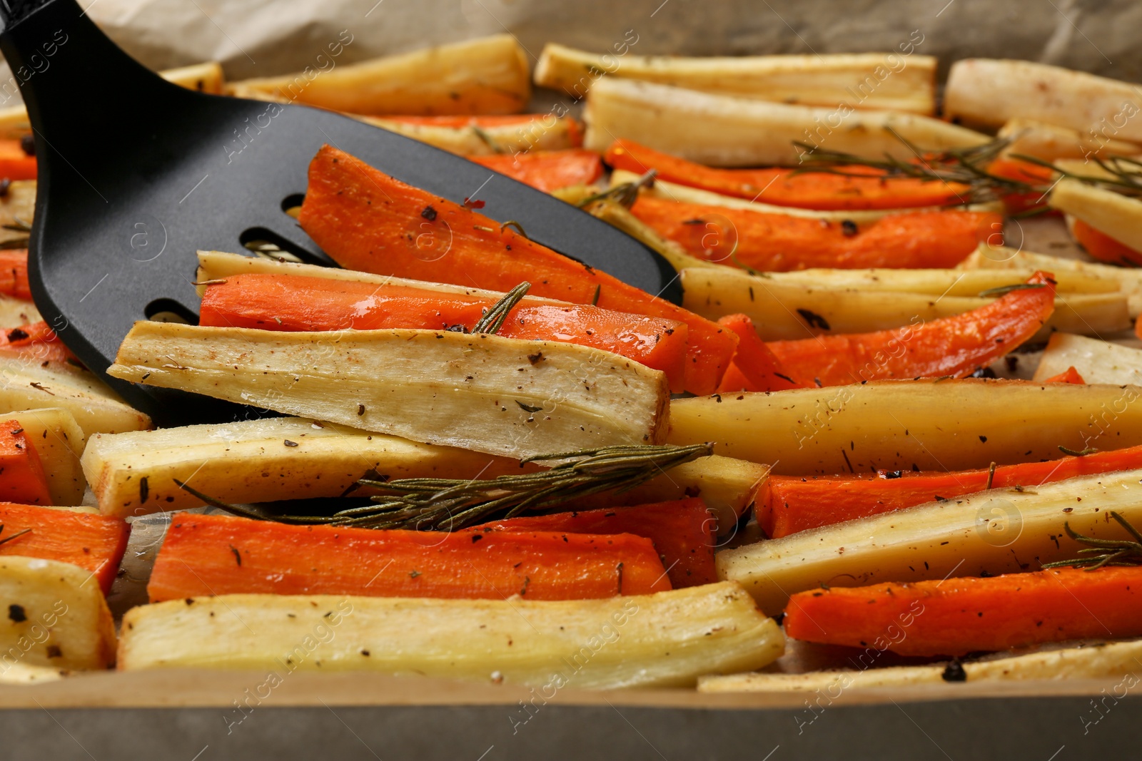 Photo of Taking baked parsnip and carrot with spatula from tray, closeup