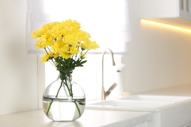 Vase with beautiful yellow chrysanthemum flowers on kitchen counter, space for text. Stylish element of interior design