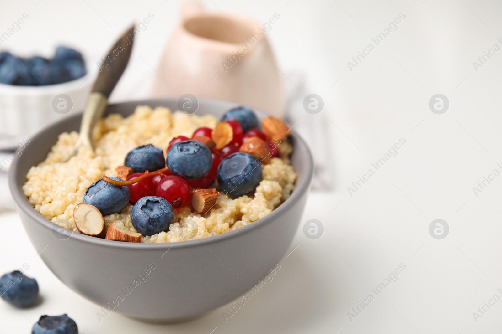 Photo of Bowl of delicious cooked quinoa with almonds, cranberries and blueberries on white table, closeup. Space for text