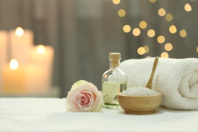 Photo of Beautiful spa composition with essential oil, sea salt and rose on white towel against blurred lights. Space for text