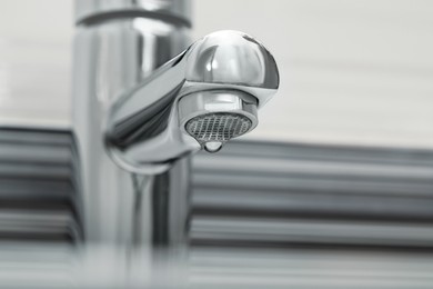 Image of Water drop falling down from tap in bathroom, closeup