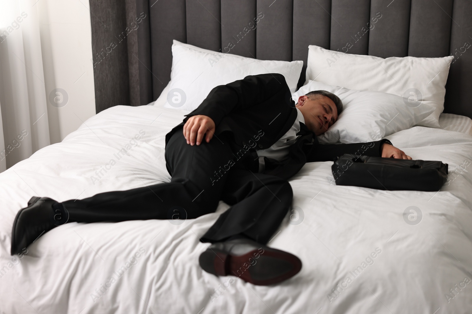 Photo of Businessman with briefcase sleeping on bed indoors