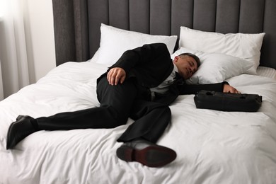 Businessman with briefcase sleeping on bed indoors