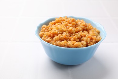 Delicious red lentils in bowl on white table, closeup. Space for text