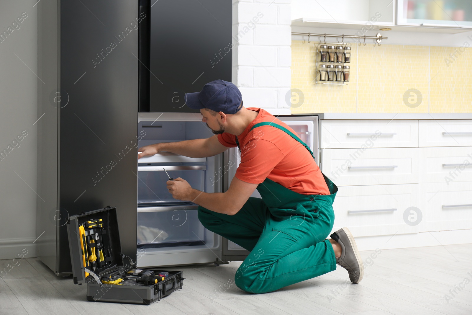 Photo of Male technician with screwdriver repairing refrigerator indoors