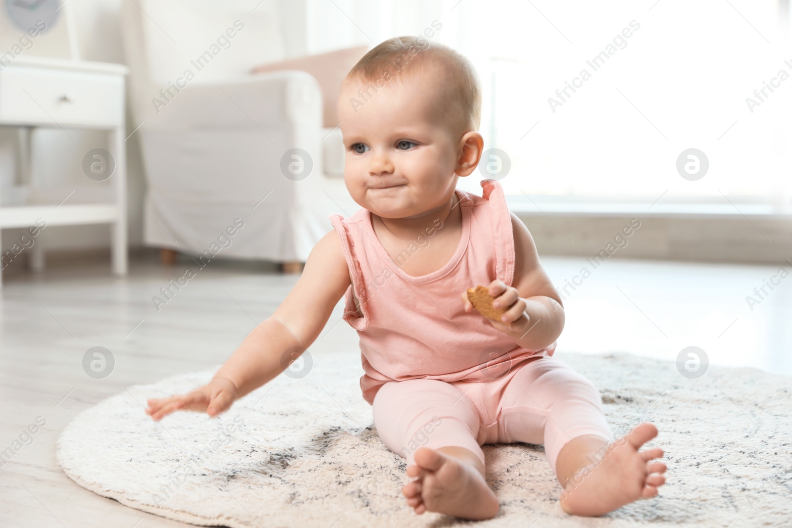 Photo of Cute baby girl with cookie on floor in room