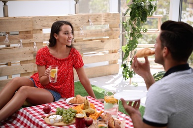 Happy couple with tasty food imitating picnic at home