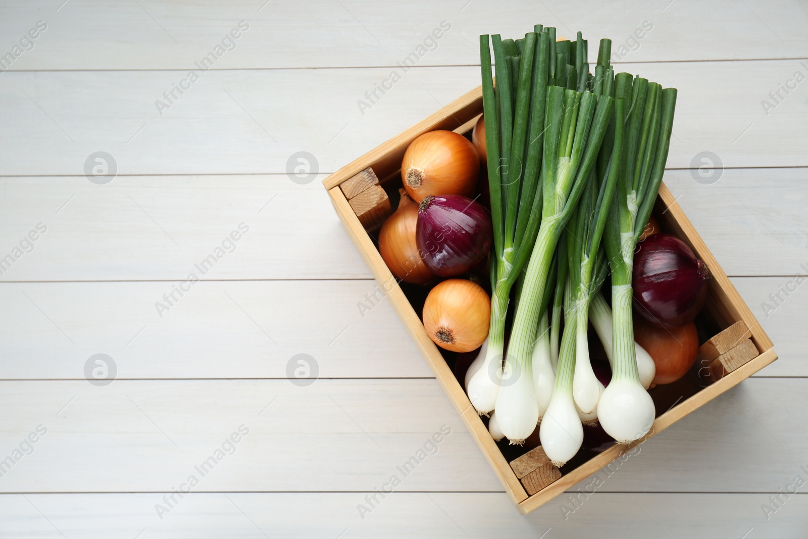 Photo of Crate with different kinds of onions on white wooden table, top view. Space for text