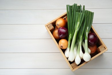 Crate with different kinds of onions on white wooden table, top view. Space for text