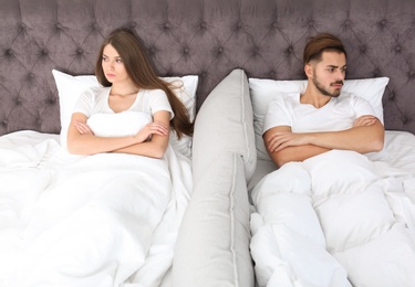 Photo of Upset young couple with relationship problems lying separately in bed at home
