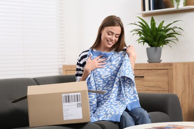 Photo of Happy woman with just unpacked new sweater at home. Online store