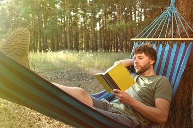 Man with book resting in comfortable hammock outdoors