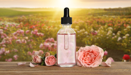 Image of Bottle of rose essential oil and flowers on wooden table against blurred background