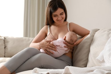 Photo of Young woman breastfeeding her little baby on sofa at home