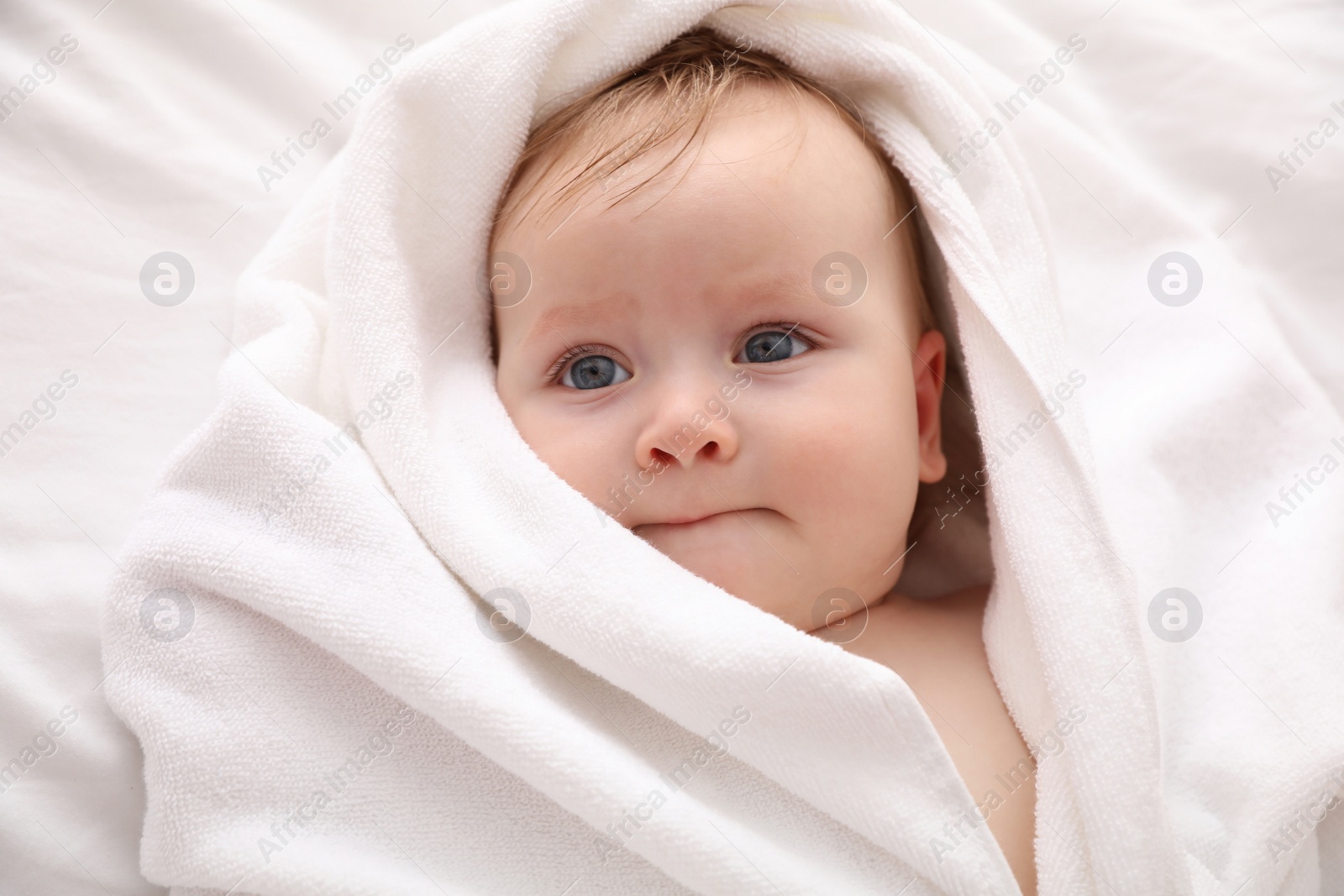 Photo of Cute little baby with soft towel lying on bed after bath, closeup
