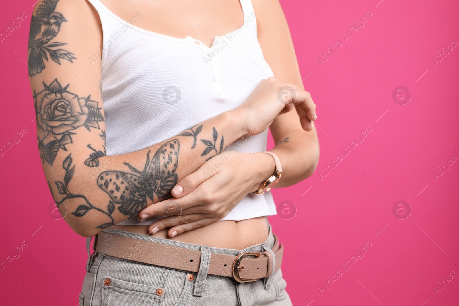 Photo of Beautiful woman with tattoos on arm against pink background, closeup