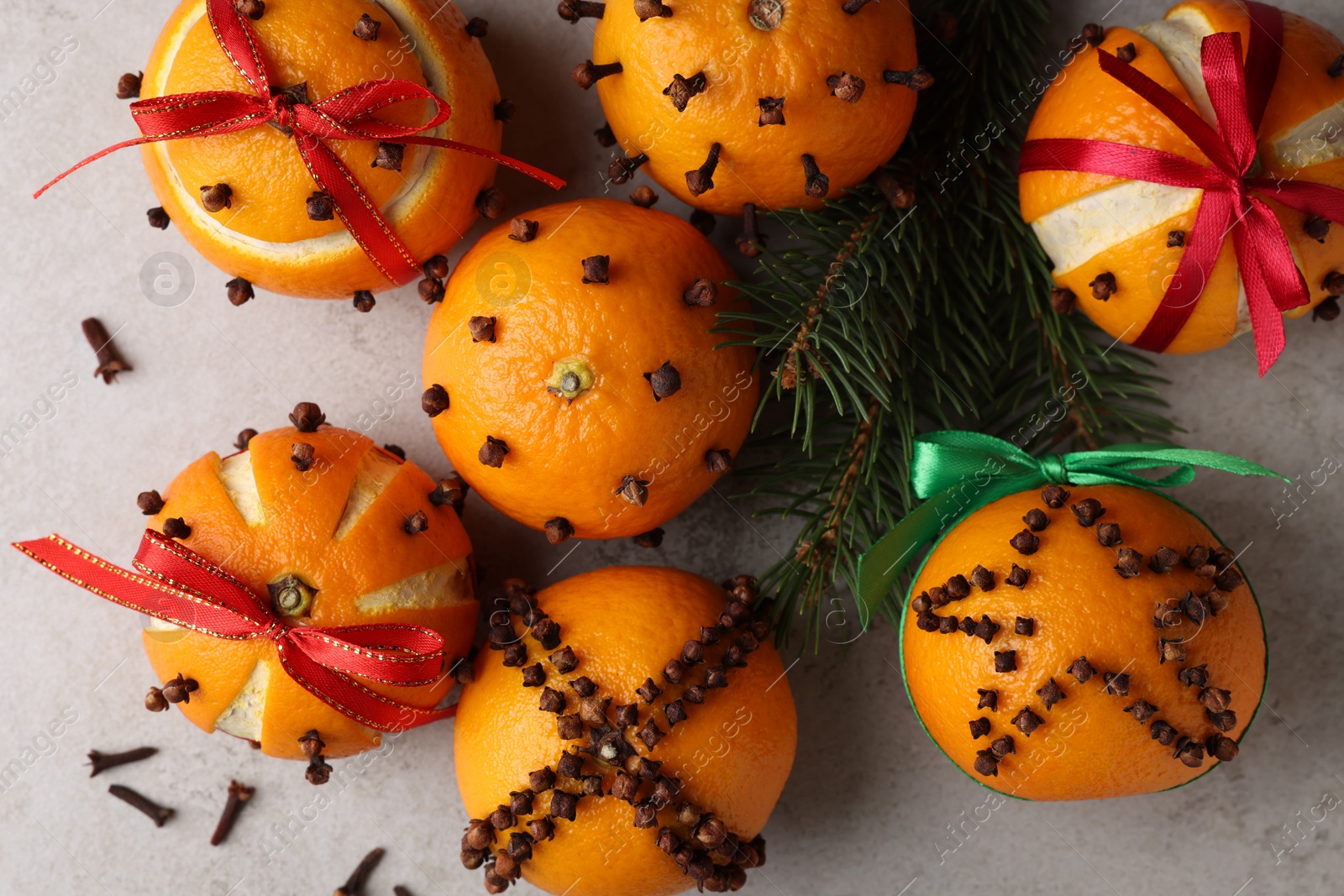 Photo of Pomander balls made of tangerines with cloves and fir branches on grey table, flat lay