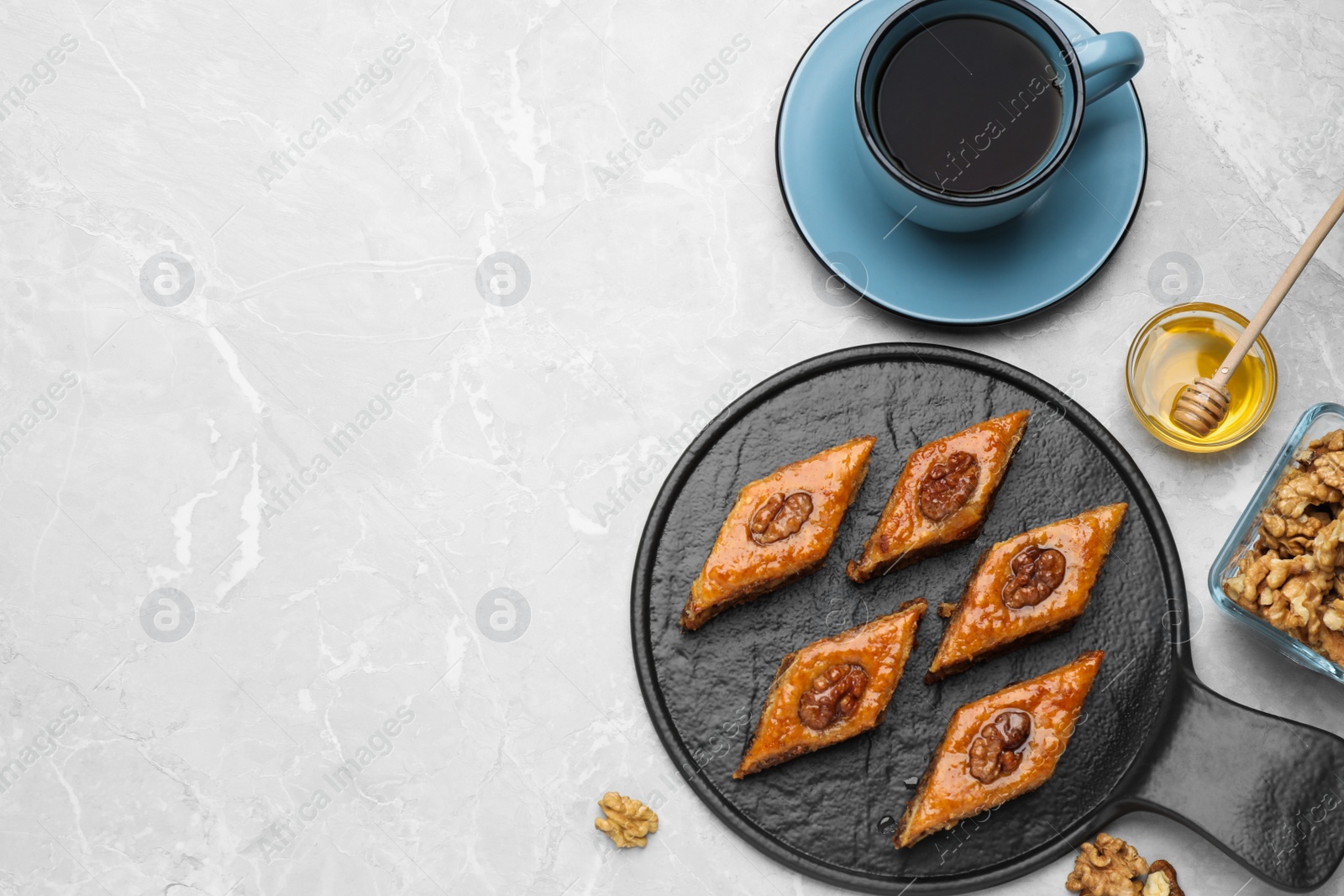 Photo of Delicious sweet baklava with walnuts, honey and hot tea on light grey marble table, flat lay. Space for text