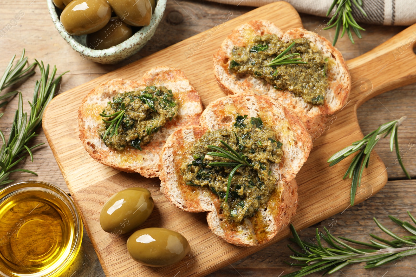 Photo of Tasty bruschettas with pesto and rosemary on wooden table, flat lay