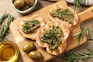 Tasty bruschettas with pesto and rosemary on wooden table, flat lay