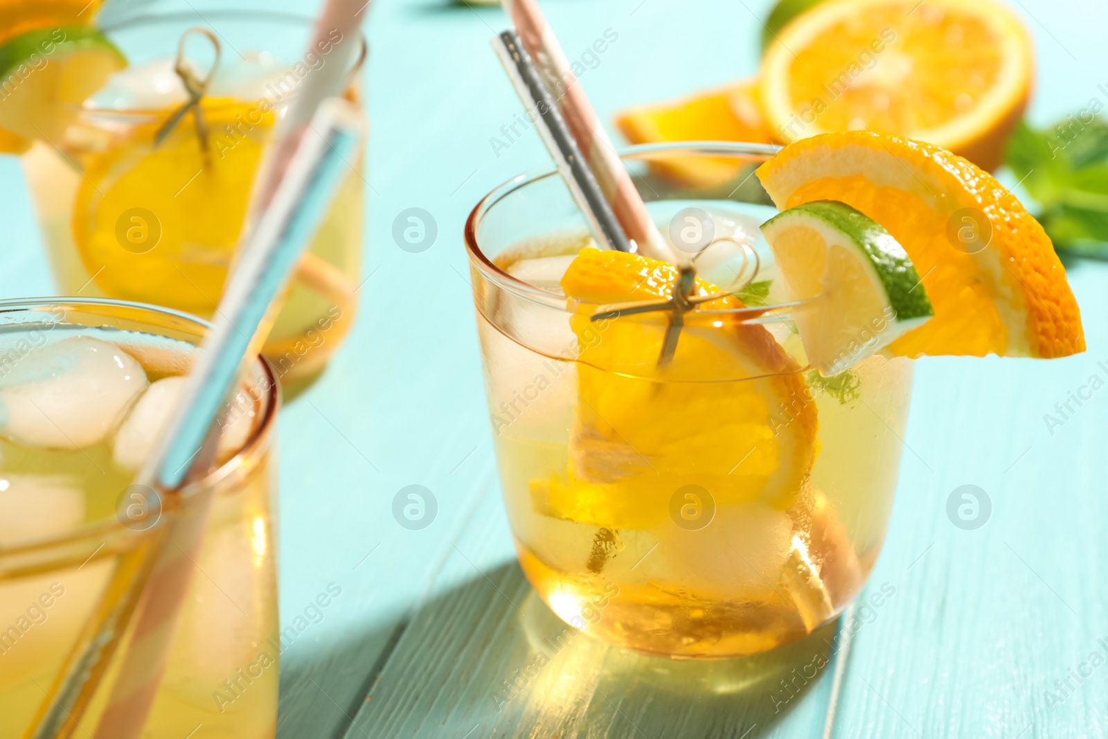 Photo of Delicious refreshing drink with orange and lime slices on light blue wooden table, closeup