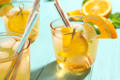 Delicious refreshing drink with orange and lime slices on light blue wooden table, closeup