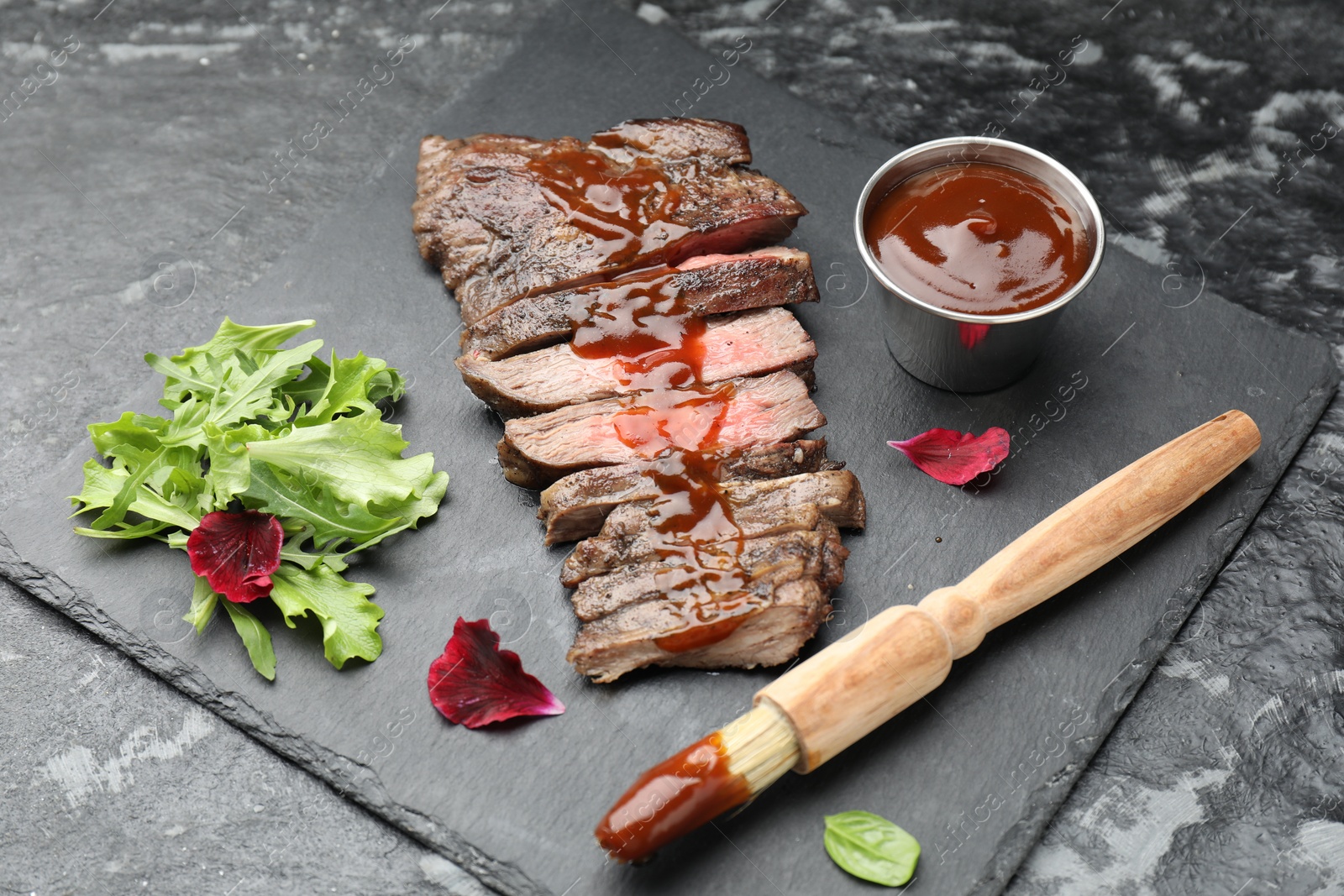 Photo of Pieces of delicious roasted beef meat with sauce and greens on black table