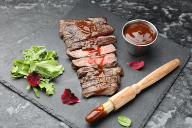 Photo of Pieces of delicious roasted beef meat with sauce and greens on black table