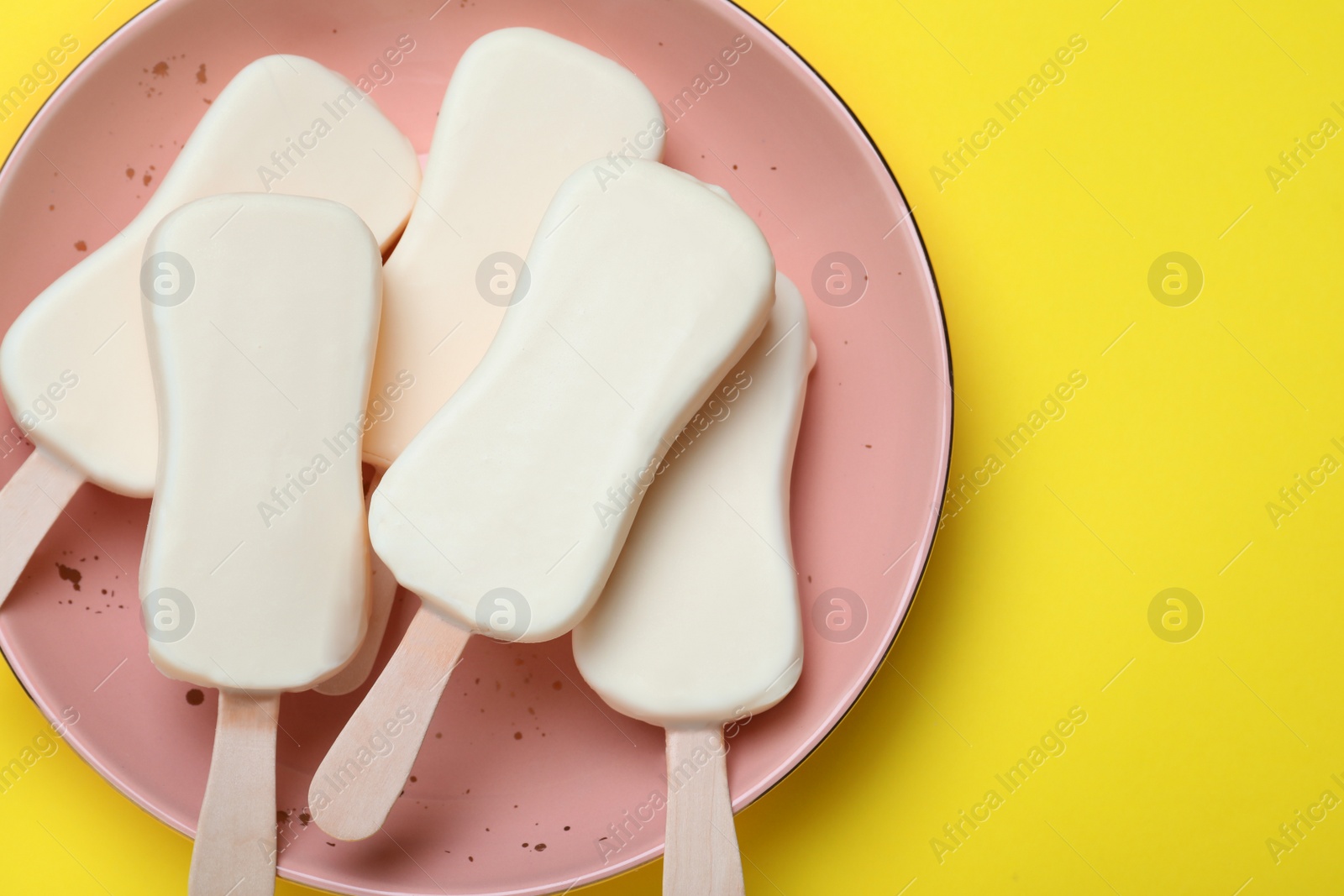 Photo of Plate with glazed ice cream bars on yellow background, top view. Space for text