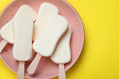 Plate with glazed ice cream bars on yellow background, top view. Space for text