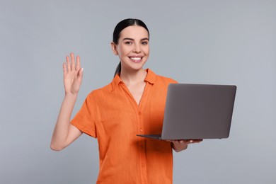 Photo of Happy woman with laptop greeting on light gray background