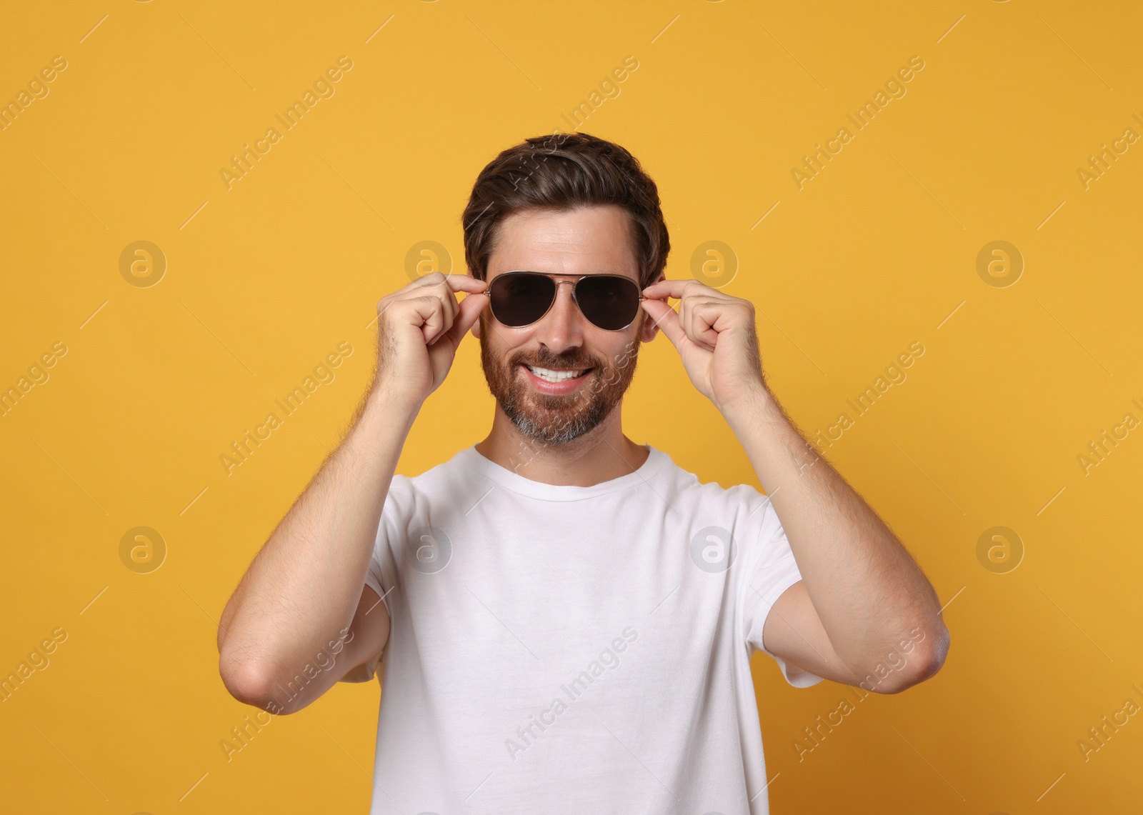 Photo of Portrait of smiling bearded man with stylish sunglasses on orange background