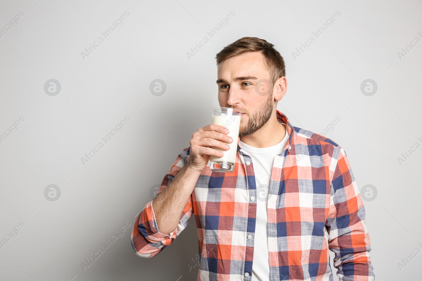 Photo of Young man drinking tasty milk on light background