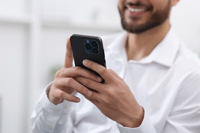 Photo of Young man using smartphone indoors, selective focus