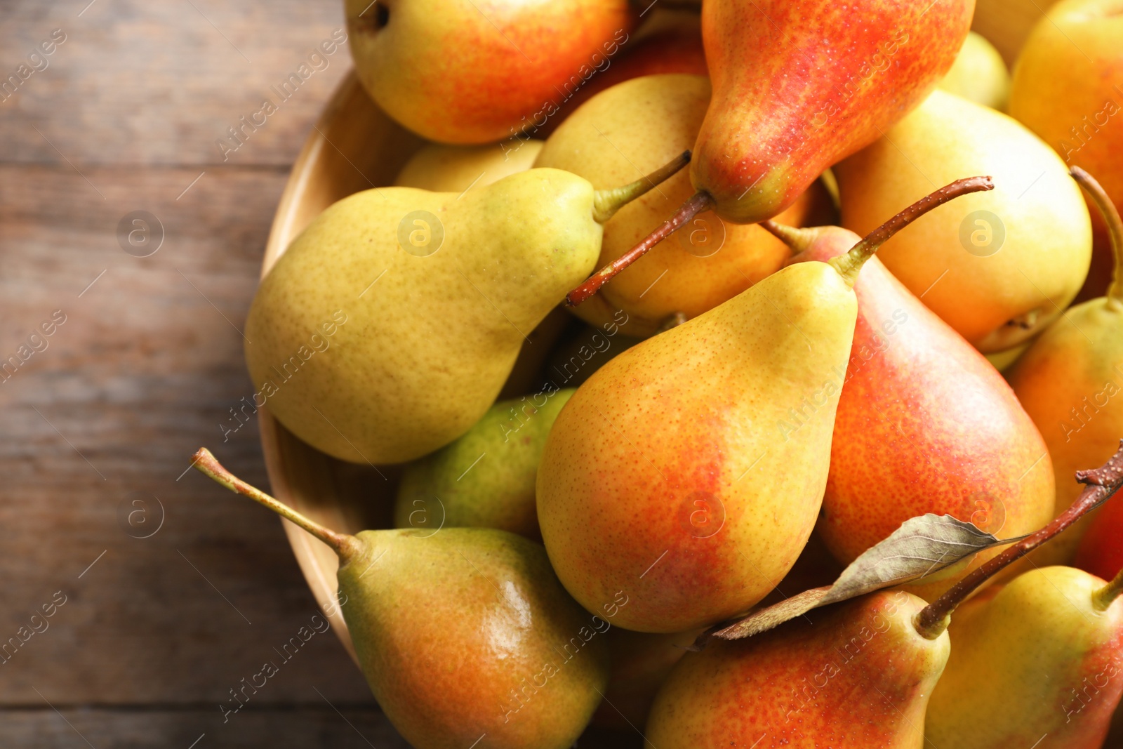 Photo of Bowl with ripe pears on wooden background, closeup