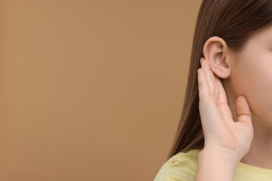 Photo of Little girl with hearing problem on pale brown background, closeup. Space for text