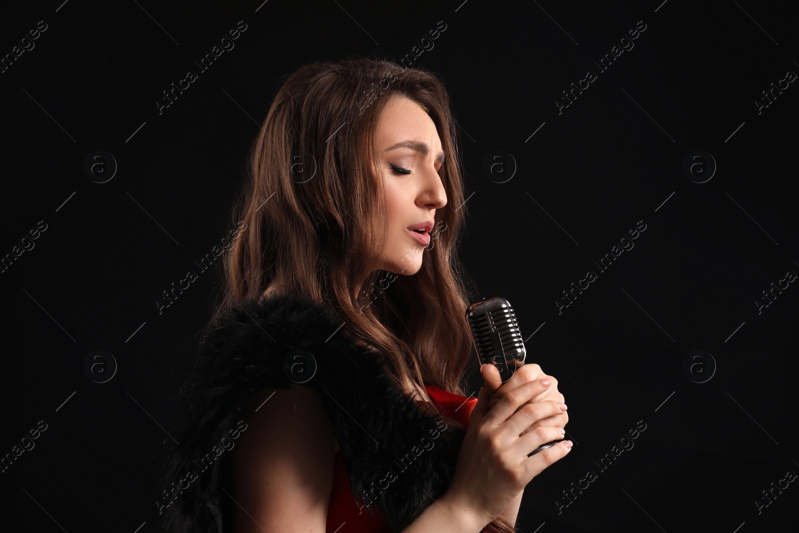 Photo of Beautiful young woman with microphone singing on black background