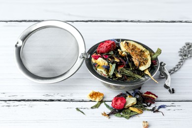 Photo of Snap infuser with dried herbal tea leaves and fruits on white wooden table, closeup