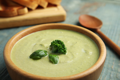 Wooden bowl of delicious broccoli cream soup with basil on table, closeup