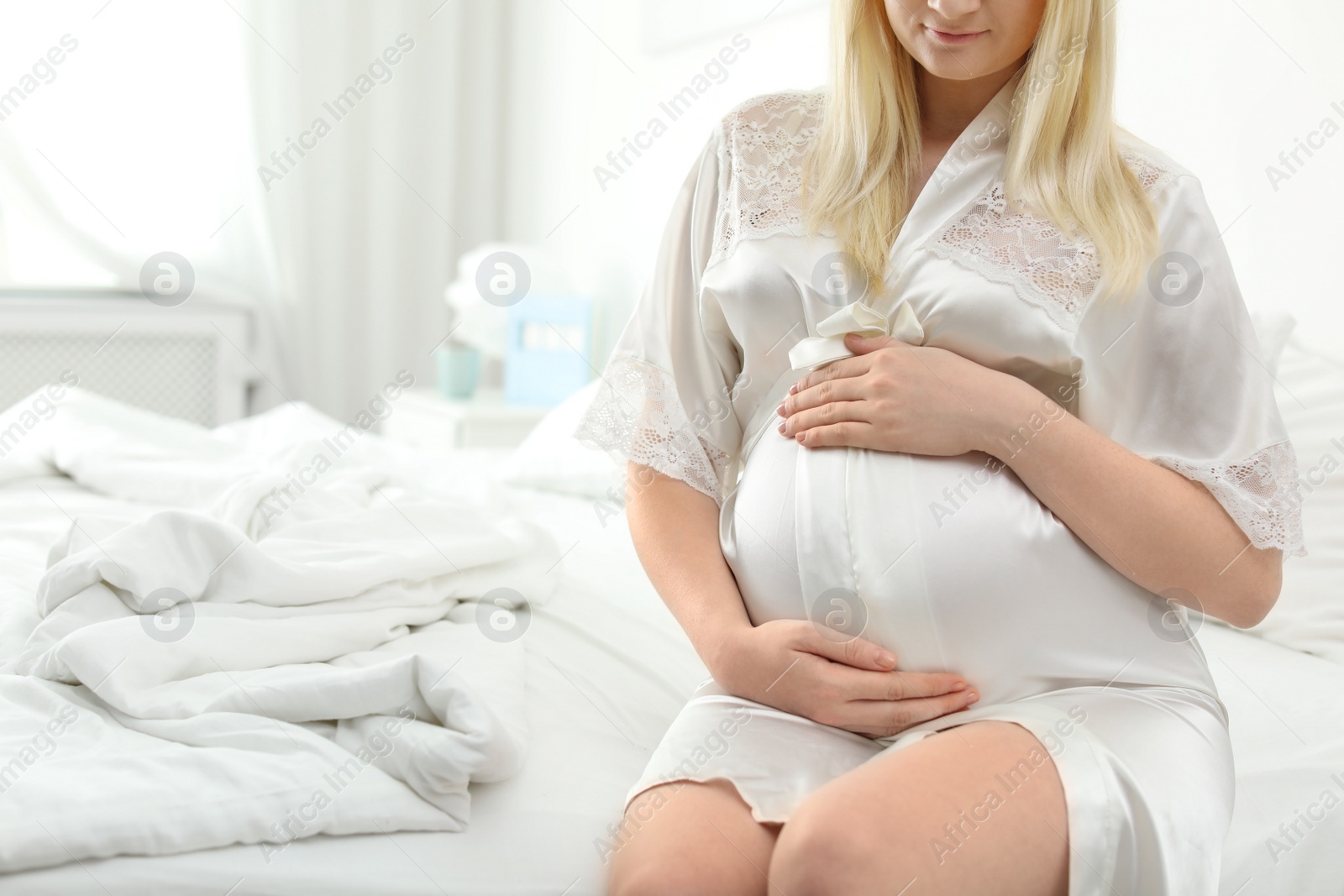 Photo of Pregnant woman sitting on bed in light room. Space for text