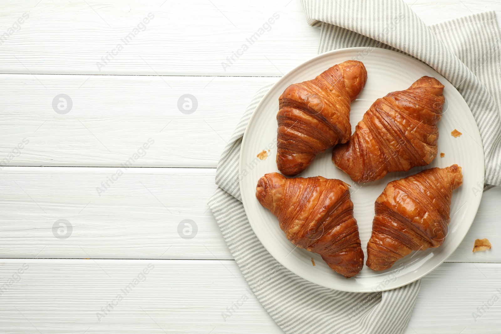 Photo of Plate with tasty croissants on white wooden table, top view. Space for text