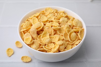 Photo of Tasty crispy corn flakes in bowl on white tiled table, closeup. Breakfast cereal