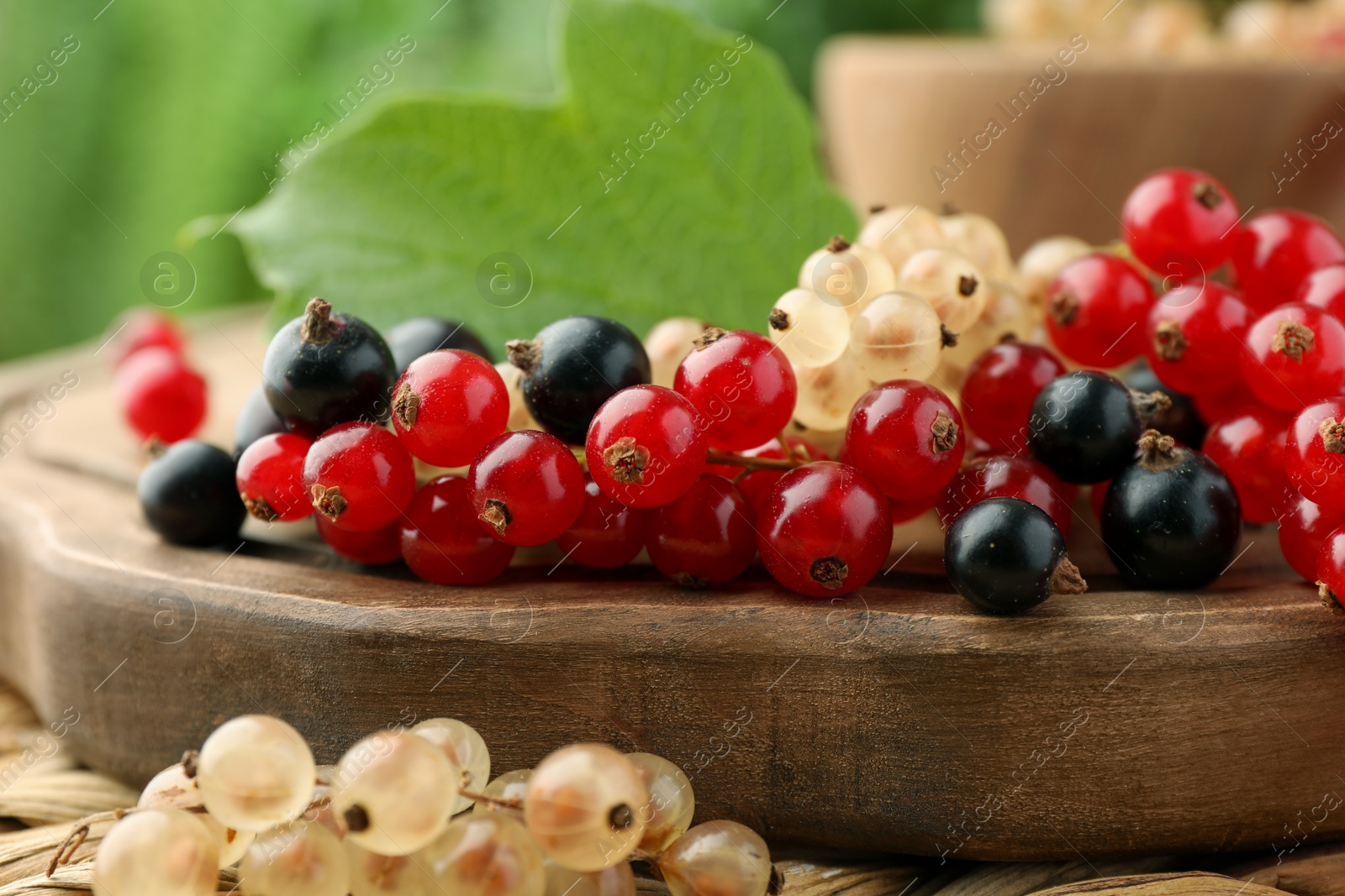 Photo of Wooden board with different fresh ripe currants and green leaf, closeup