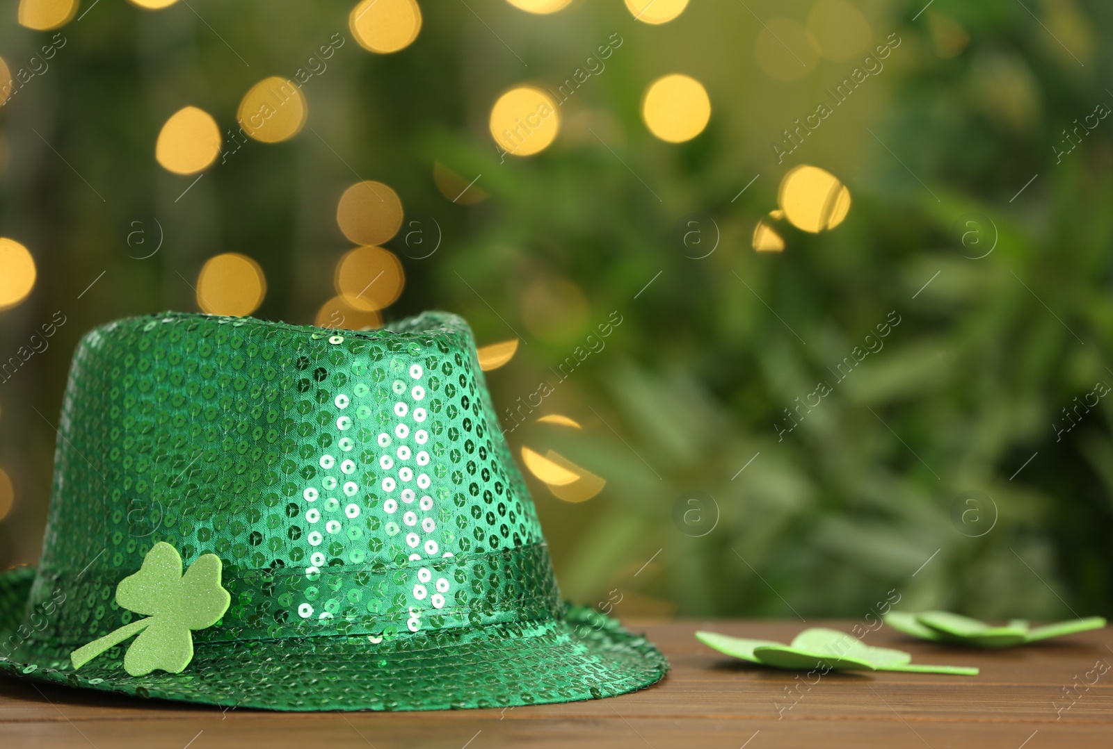 Photo of Green sequin hat with clover leaf on wooden table against blurred lights, space for text. St Patrick's Day celebration