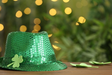 Photo of Green sequin hat with clover leaf on wooden table against blurred lights, space for text. St Patrick's Day celebration