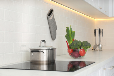 Photo of Pot on stove and fresh vegetables in modern kitchen