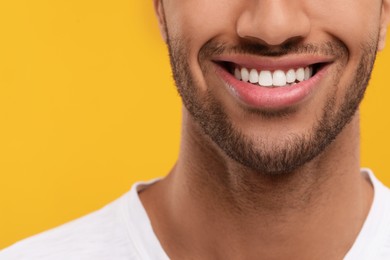 Photo of Smiling man with healthy clean teeth on orange background, closeup. Space for text