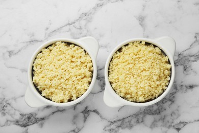 Photo of Bowls with tasty couscous on white marble table, flat lay