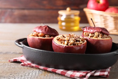 Photo of Tasty baked apples with nuts in baking dish on wooden table, closeup